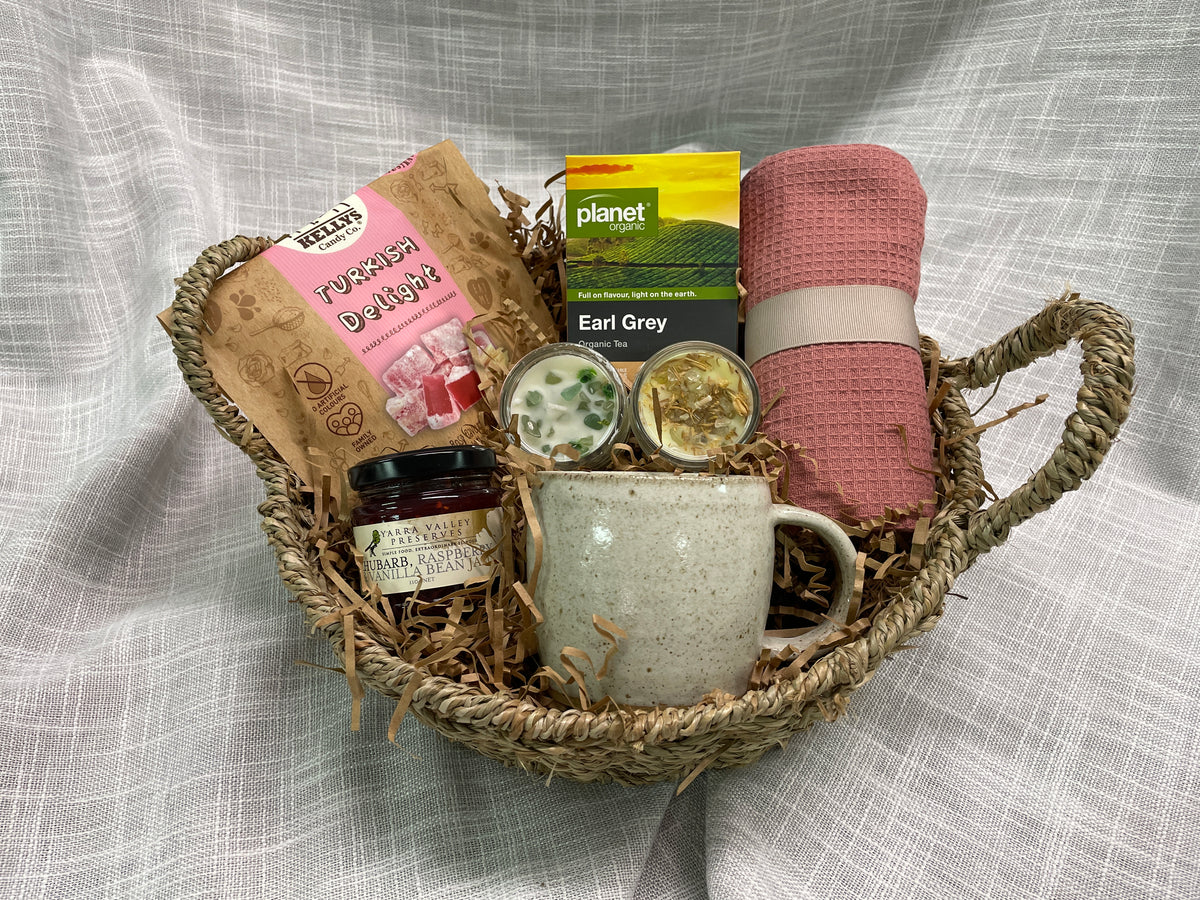 Seagrass basket featuring pottery mug, turkish delight, jam, tea, tea towel and 2 miniature candles.