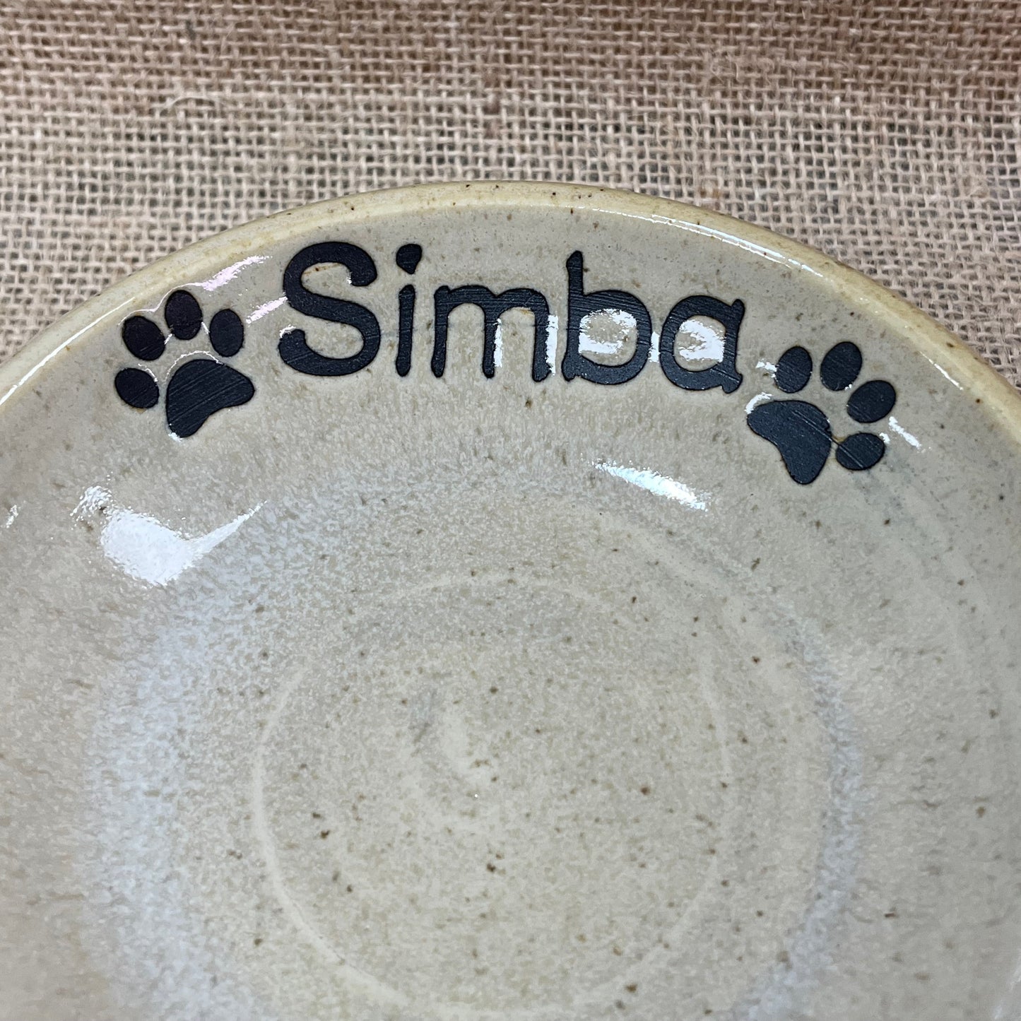 Ceramic plate with 'Simba' and paw prints on a textured surface