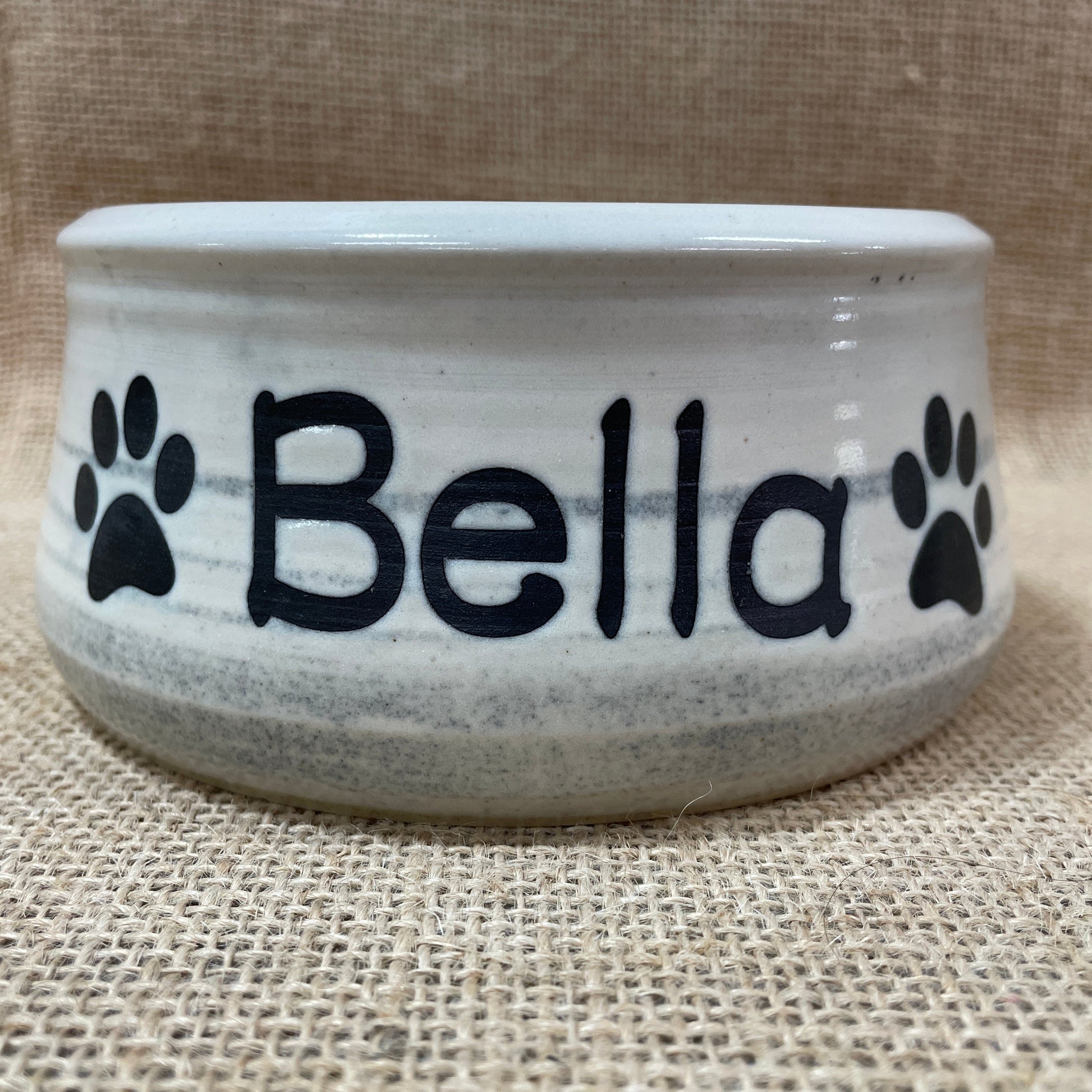 White pet bowl with 'Bella' and paw prints on a beige background