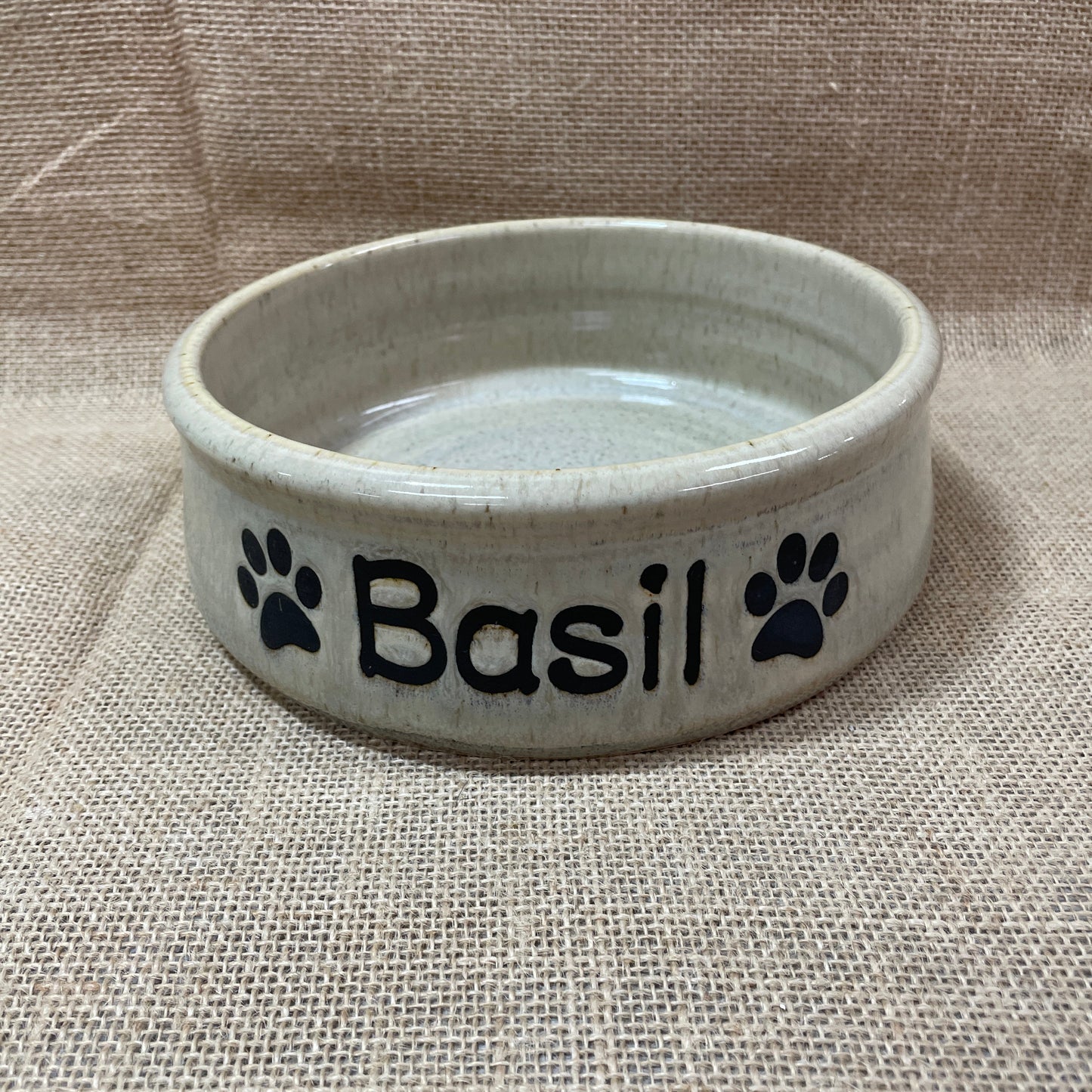 Ceramic pet bowl with 'Basil' and paw prints on a textured surface