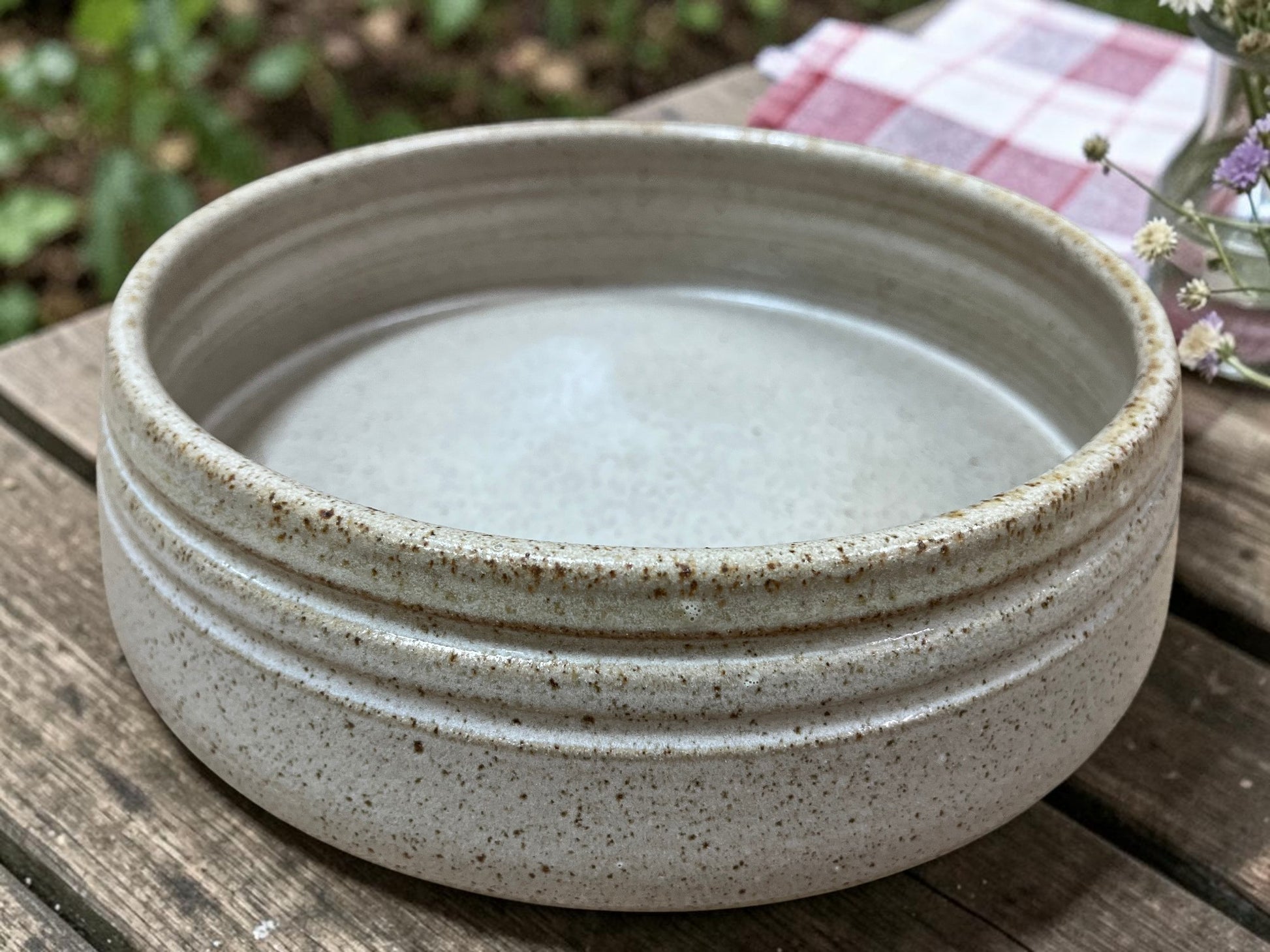 Speckled ceramic bowl on a wooden surface with a natural background