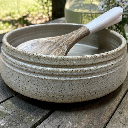 Speckled ceramic bowl with a wooden spoon on a wooden table outdoors