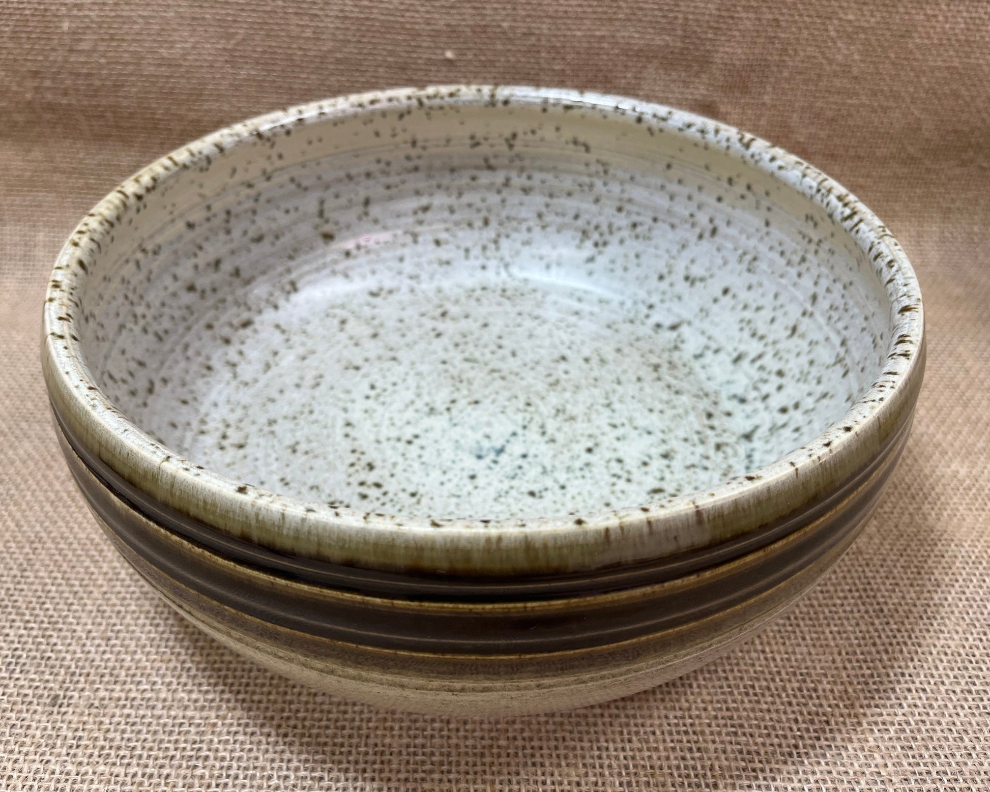 Stack of ceramic bowls with speckled texture on a beige fabric background