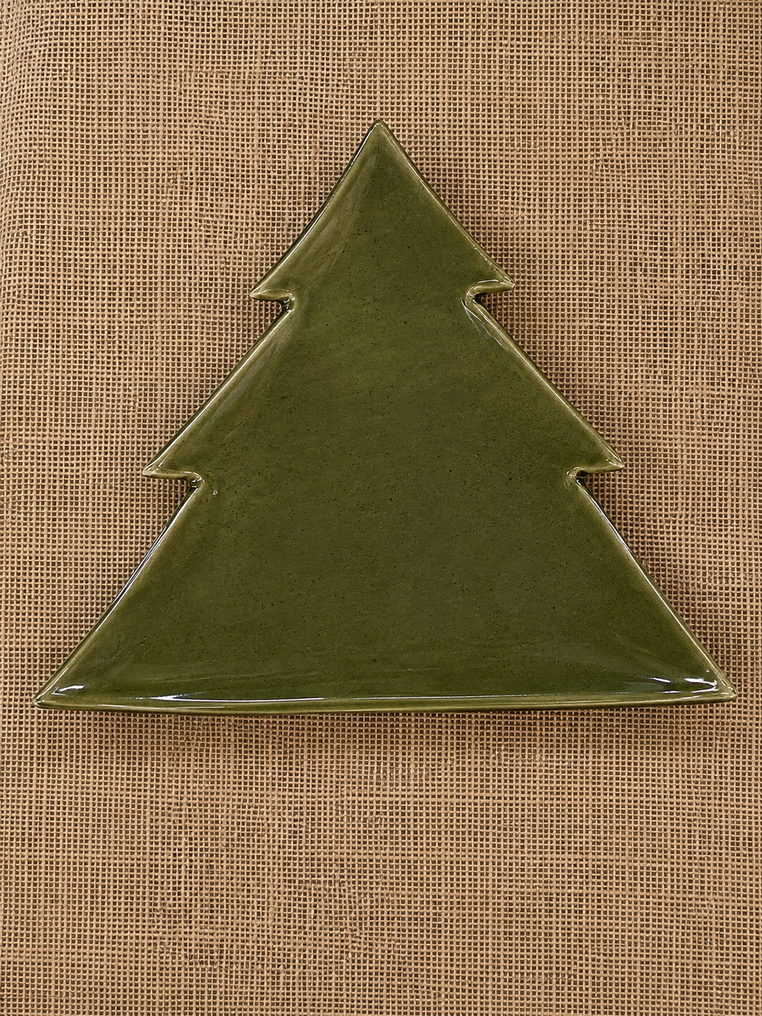 A glossy olive green ceramic plate shaped like a Christmas tree, displayed on a textured brown burlap background.