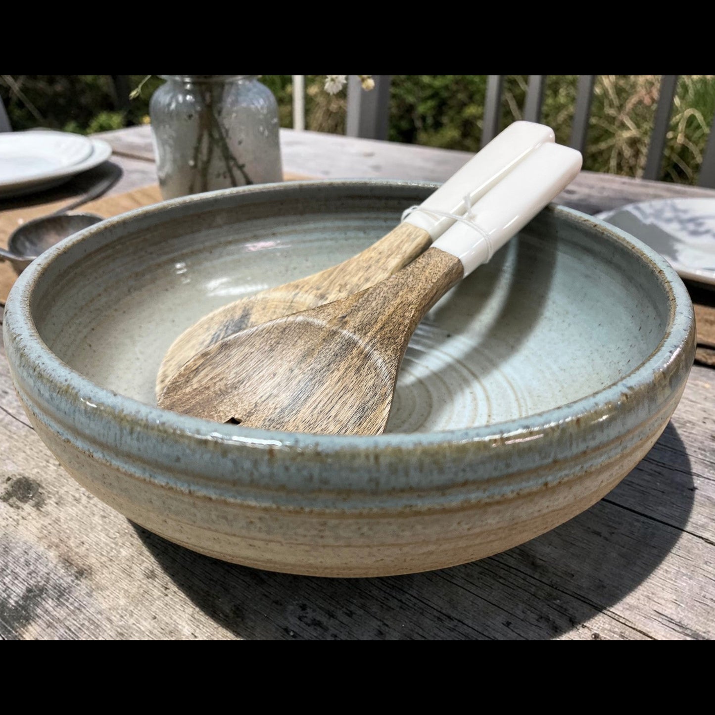 Ceramic bowl with wooden spoon on a wooden table outdoors