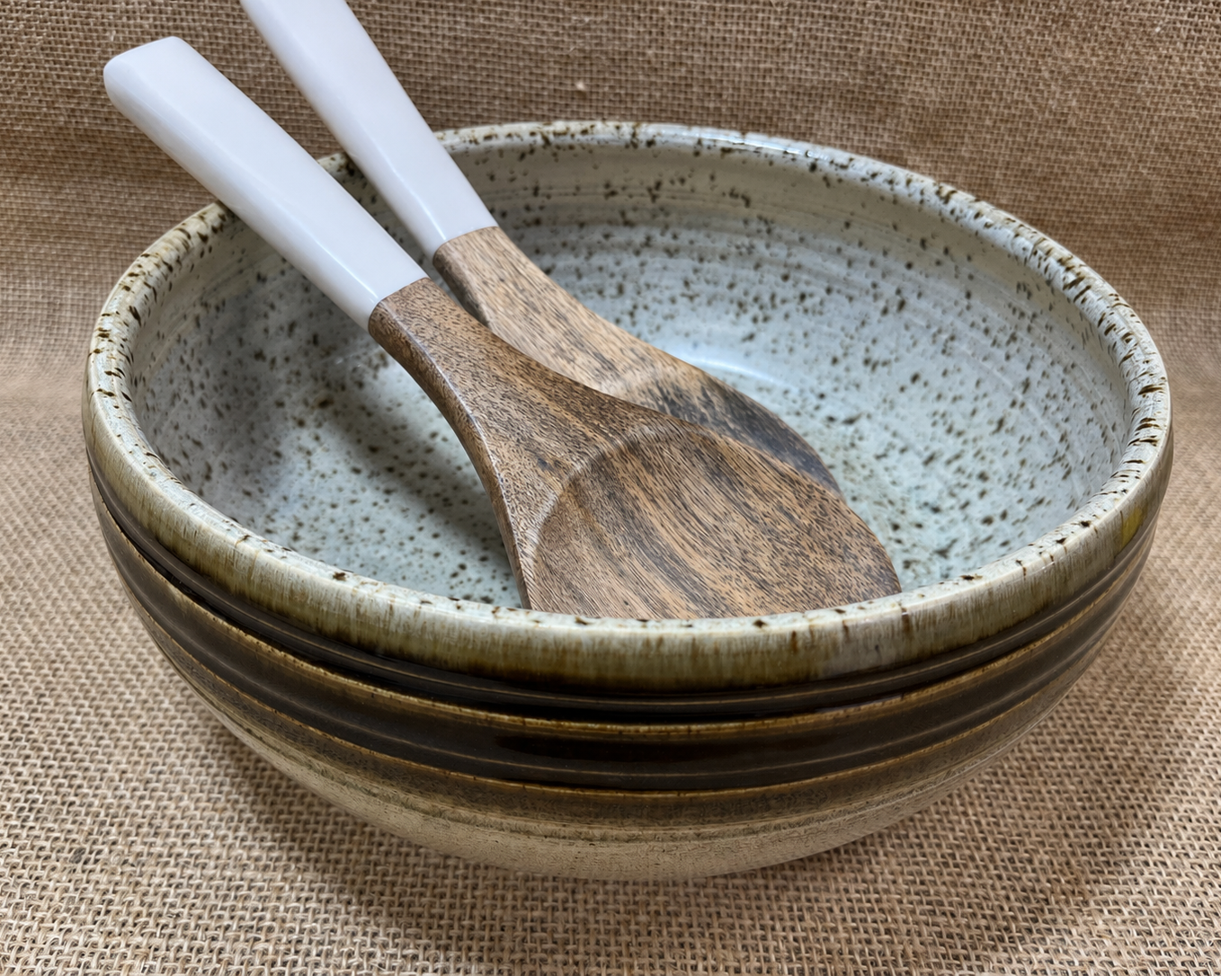 Ceramic bowl with speckled texture and wooden spoon on a textured fabric background