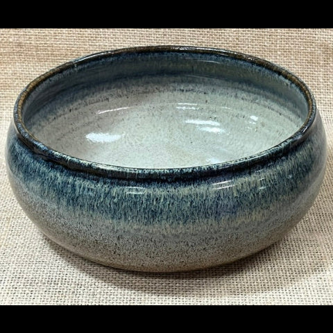 A round ceramic bowl with a blue and gray glaze, resting on a textured beige fabric background.