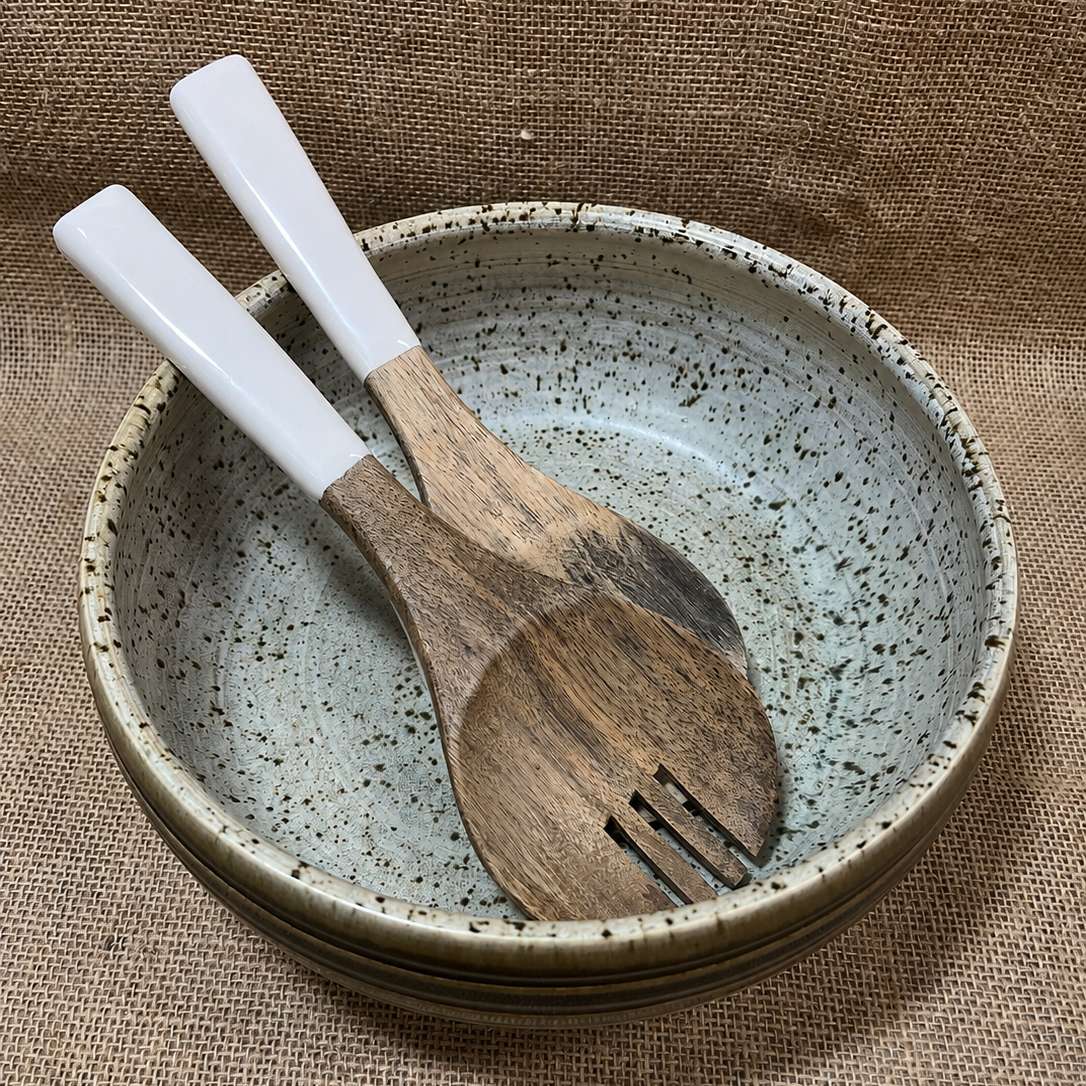 Speckled ceramic bowl with wooden utensils on a textured brown background