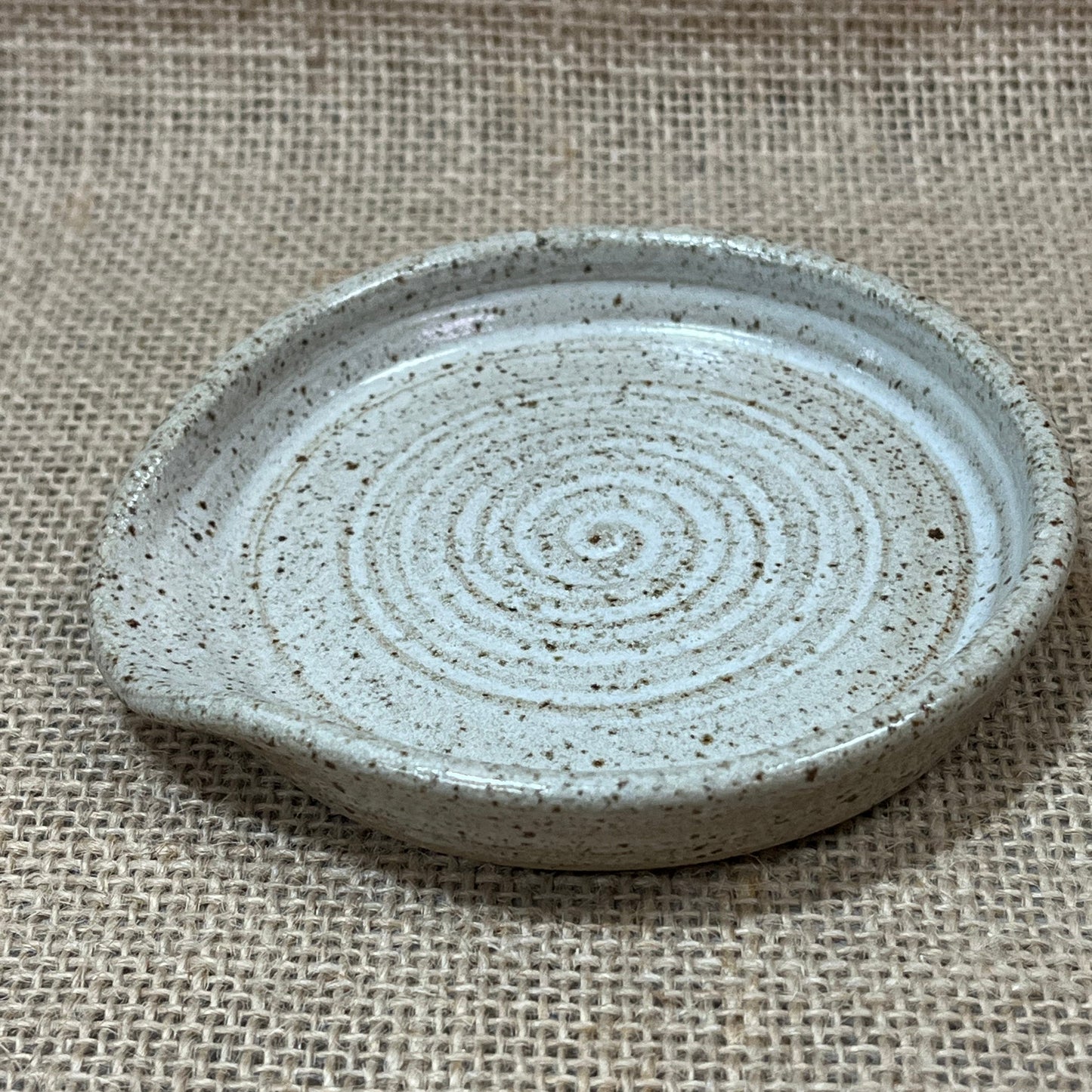 Round ceramic dish with concentric circle pattern on a textured beige fabric background