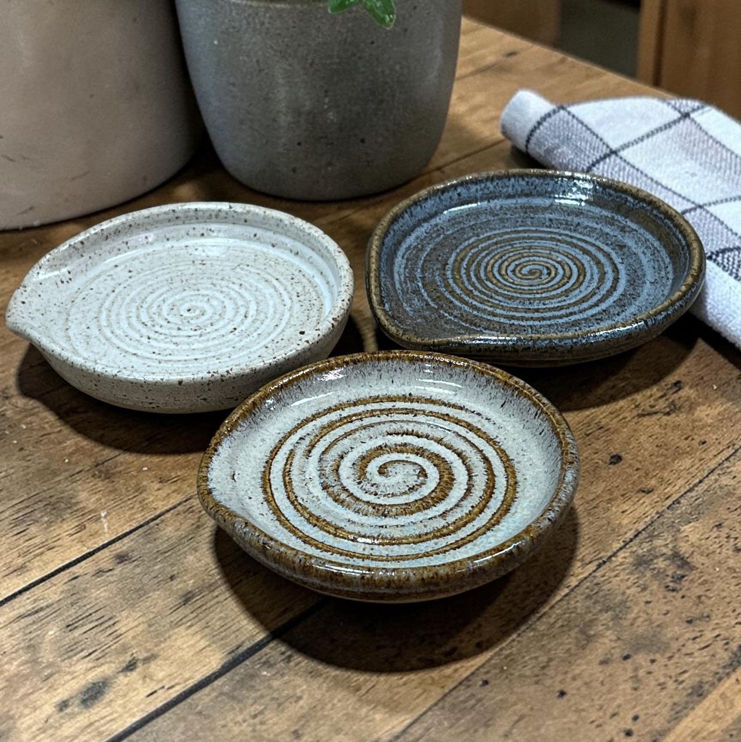 Three ceramic plates with spiral patterns on a wooden surface, with a plant and towel in the background.
