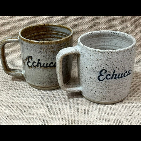 Two ceramic mugs with the word 'Echuca' printed on them, displayed on a textured beige burlap background. One mug is speckled light gray with dark gray/black lettering, and the other is a rustic brownish-gray speckled mug with the same text in dark brown.