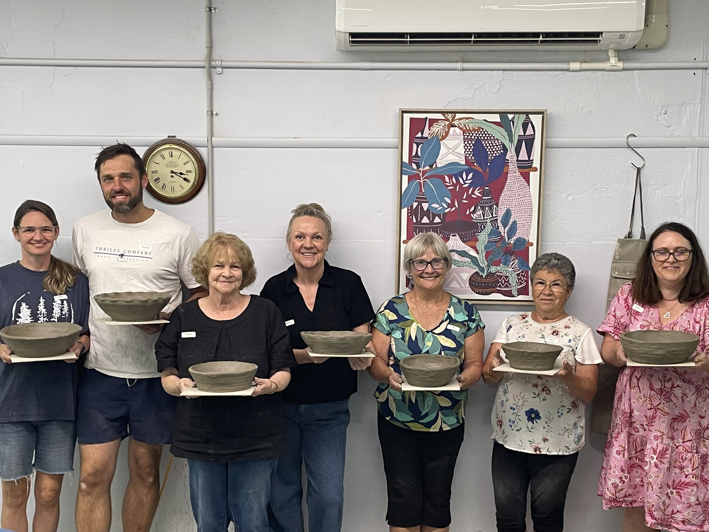 Group of people holding ceramic bowls in a pottery studio.