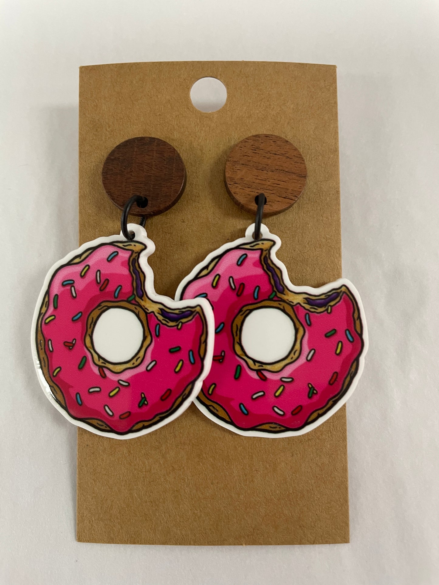 Pink iced donut resin dangle earrings with a bite taken out and natural timber stud tops by Beldari Pottery.